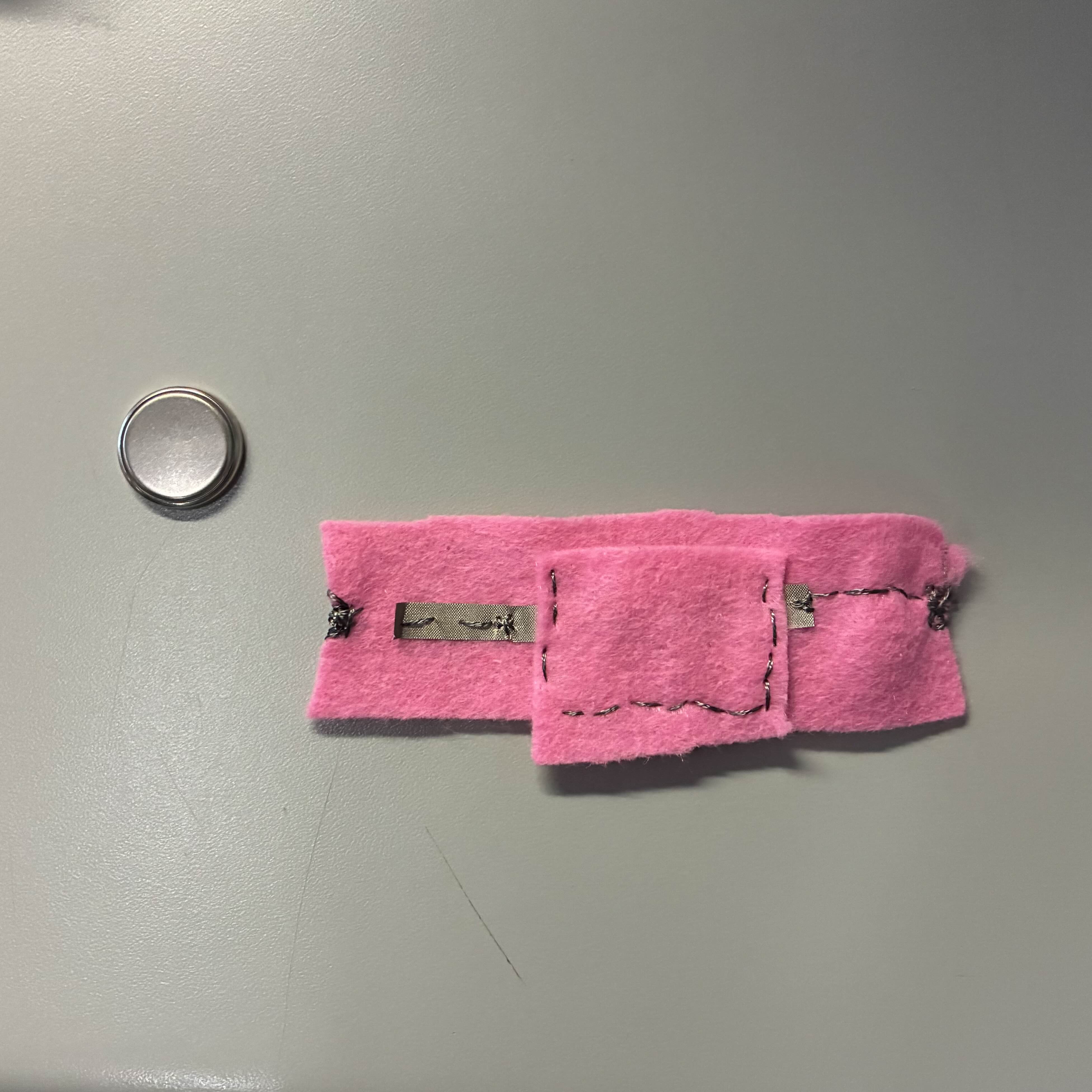 This was the 'finished' product with the battery beside it. I used conductive thread to stitch the felt together and I put the conductive material underneath the pocket.