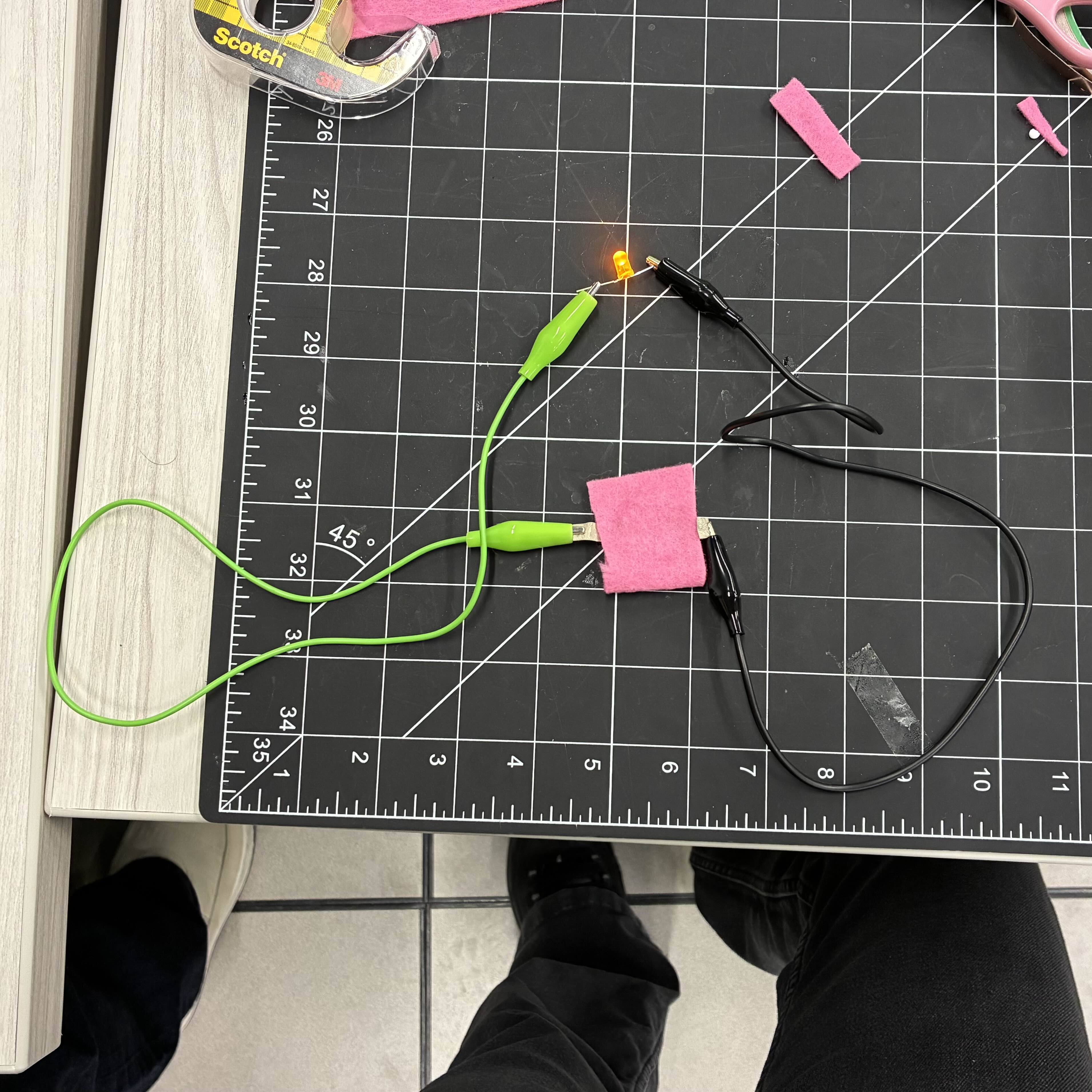 This is my completed battery pocket. I attached alligator clip wires to the conductive fabric to the LED light. I chose to use a yellow LED light since I hadn't used that colour yet and it because it would contrast the black background.