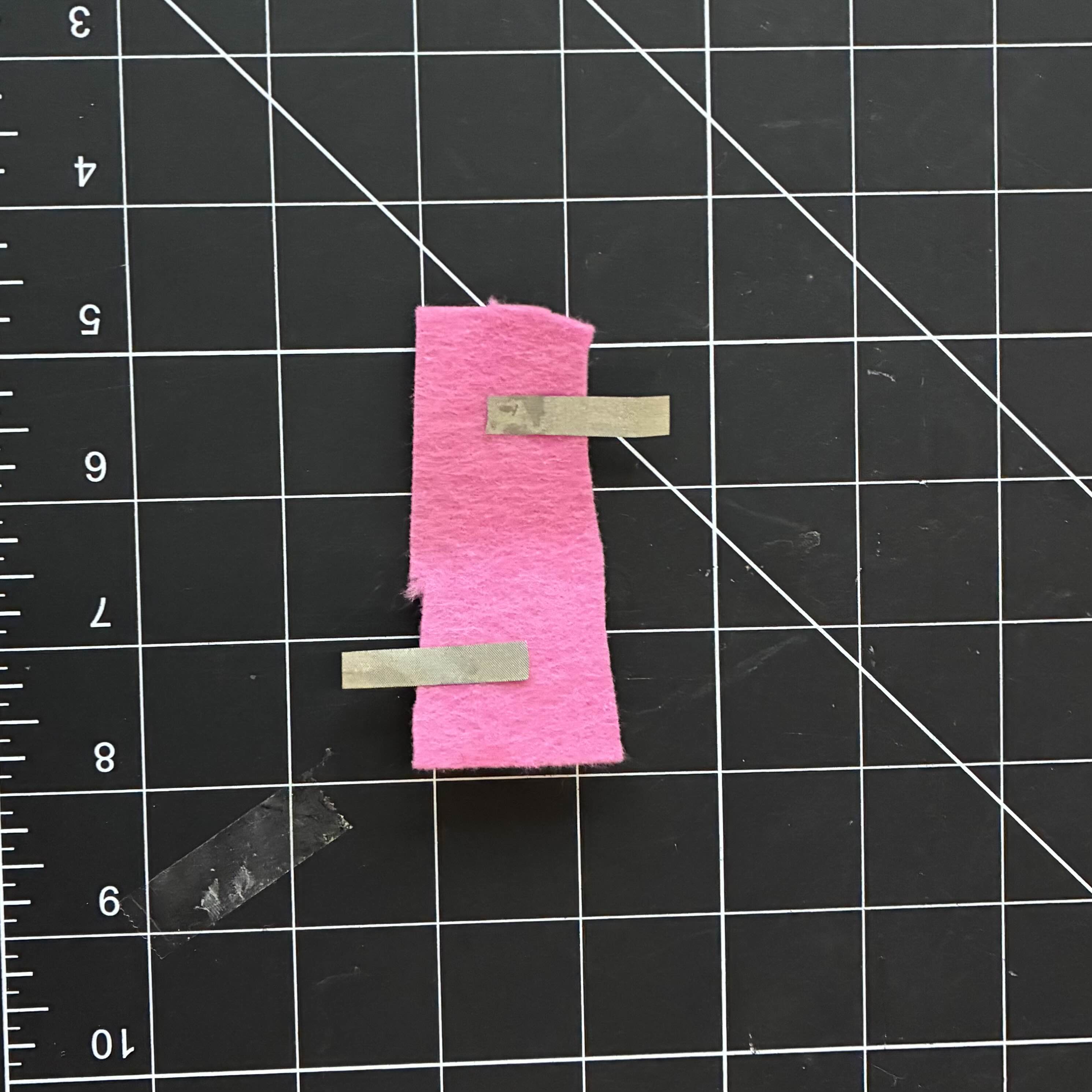 This is my attempt at making a smaller battery holder with conductive fabric. I glued two strips of conductive fabric to a pink, rectangular, piece of felt.